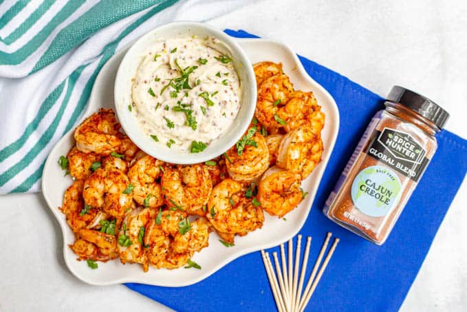 Spicy roasted shrimp served on a white plate alongside toothpicks and a Cajun seasoning blend