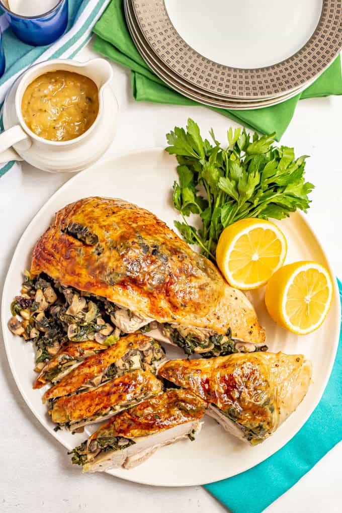 A browned roasted turkey breast stuffed with spinach and mushrooms, served on a white platter