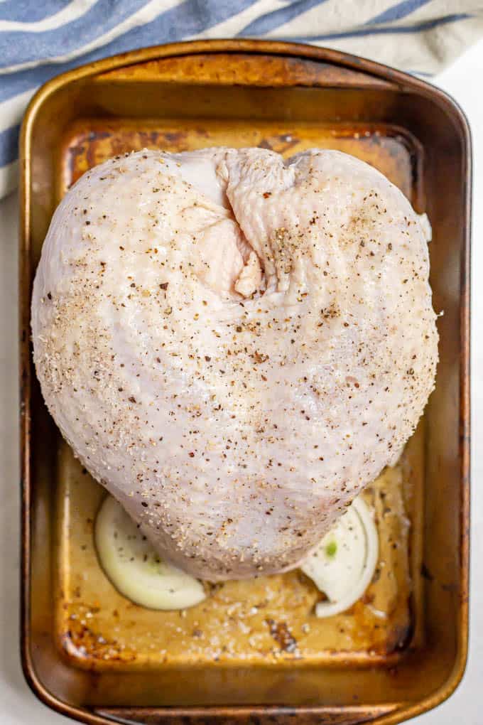 A raw turkey breast in a roasting pan that's been seasoned with salt and black pepper