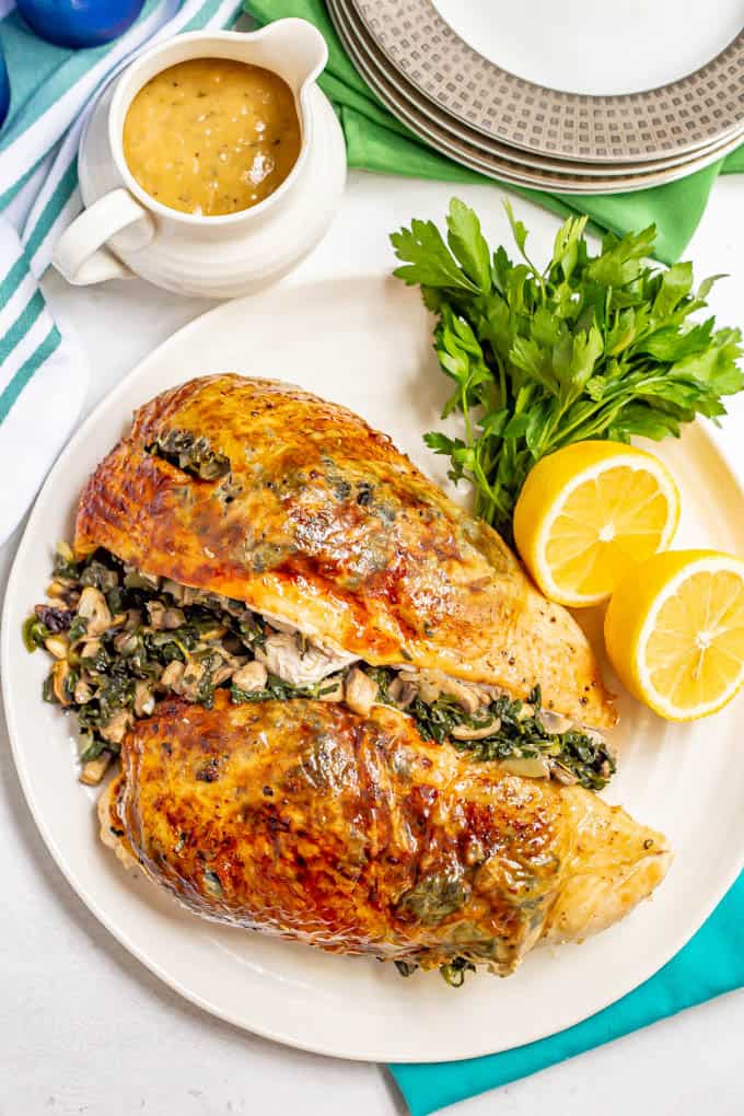 Two roasted, browned turkey breast halves with spinach mushroom stuffing presented on a white platter with parsley and lemon