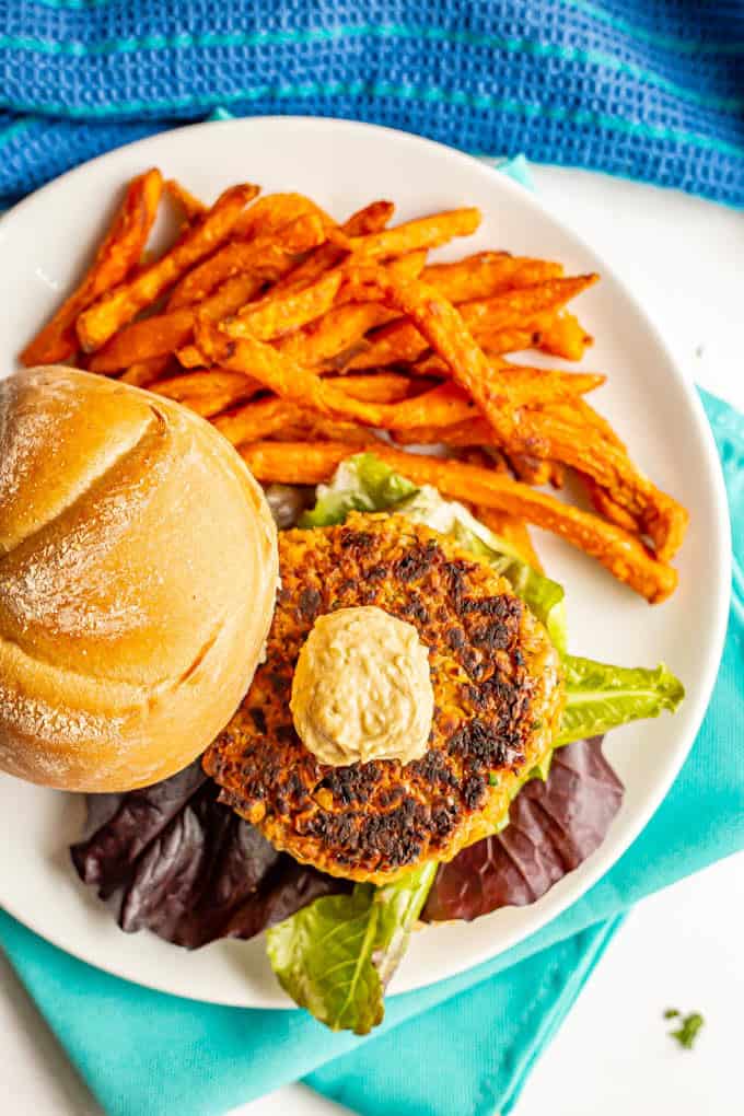 Golden brown chickpea burger served on a bun with lettuce and hummus and a side of sweet potato fries