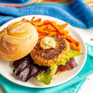 Golden brown chickpea burger served with lettuce and hummus and a side of sweet potato fries