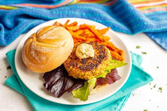 Golden brown chickpea burger served with lettuce and hummus and a side of sweet potato fries