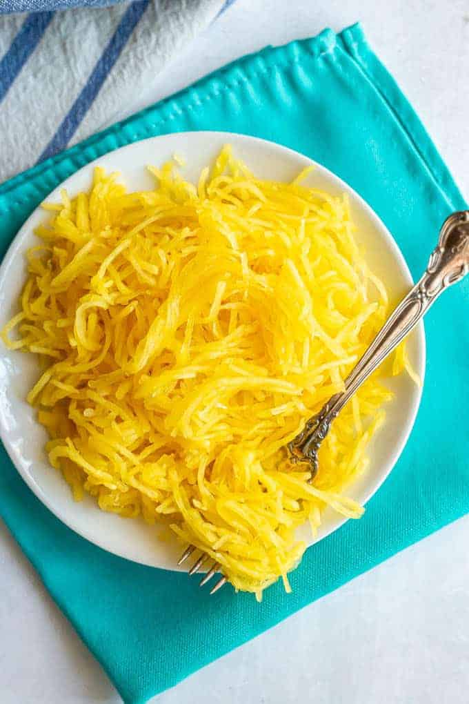 Strands of spaghetti squash served on a white plate with a fork twirled in them
