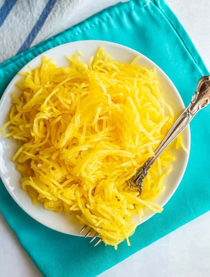 Strands of spaghetti squash served on a white plate with a fork twirled in them
