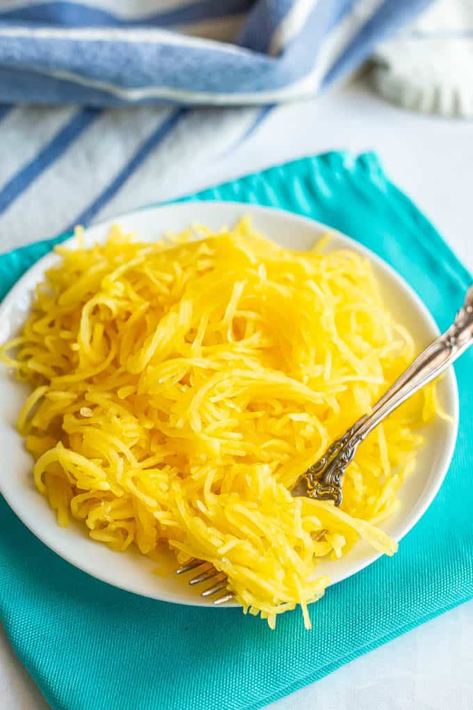 Strands of spaghetti squash served on a white plate with a fork twirled in them