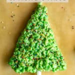 Close up of a Christmas tree shaped green Rice Krispie treat with sprinkles on it and a white pretzel rod tree trunk in the bottom.