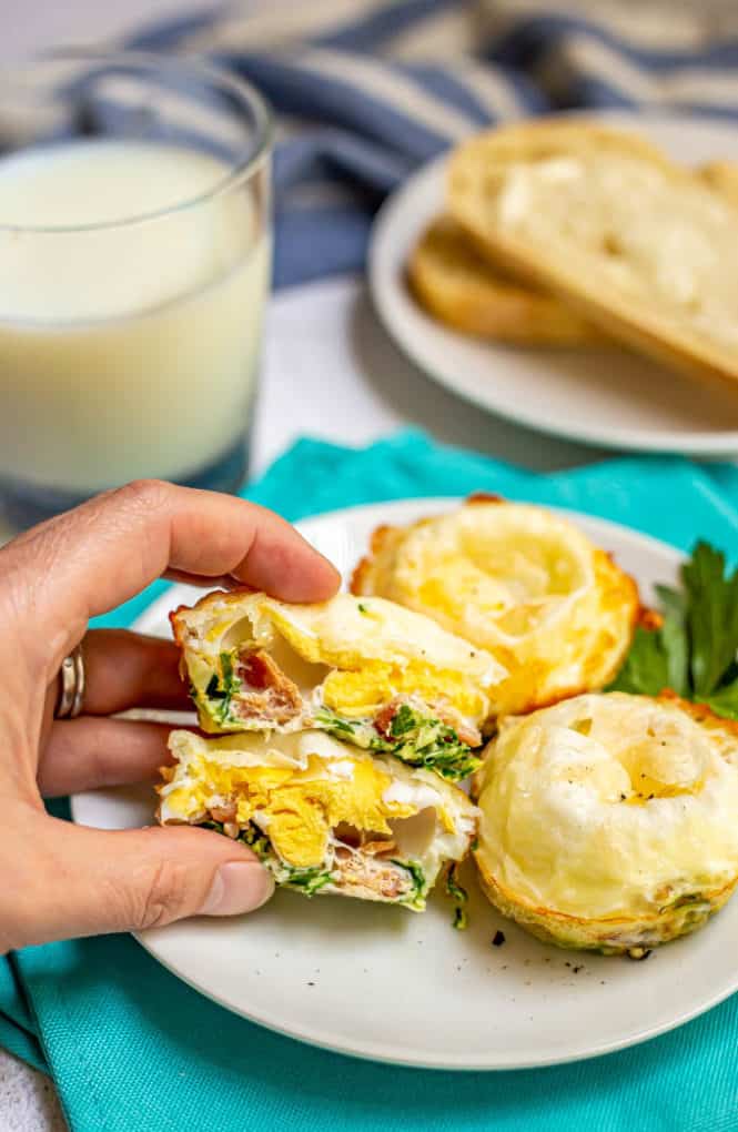 A baked egg muffin cut in half and held to show the cooked egg yolk, spinach and bacon filling