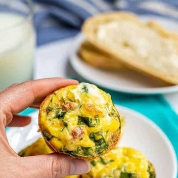 A hand holding up a breakfast egg muffin from a plate