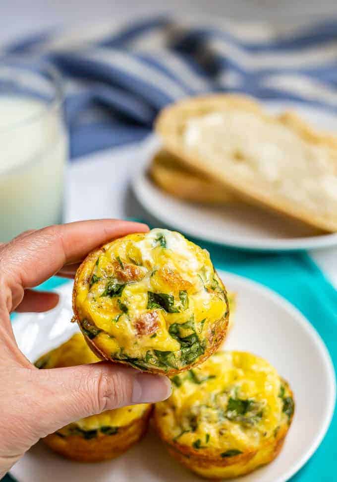 A hand holding up a breakfast egg muffin from a plate