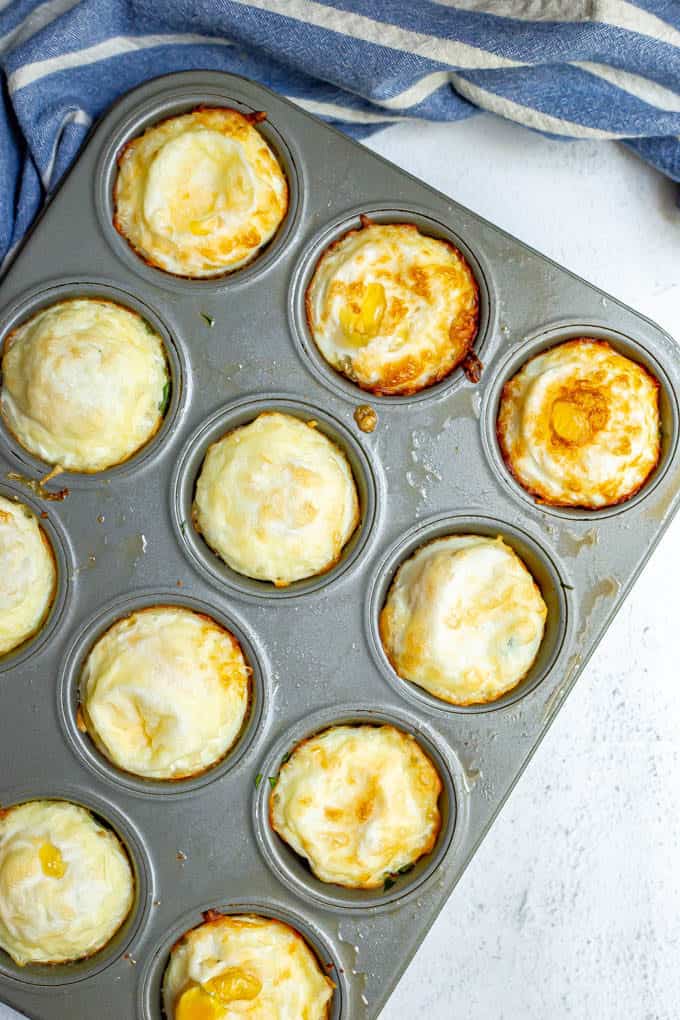 Baked egg muffin cups in a muffin tray with a blue striped towel underneath