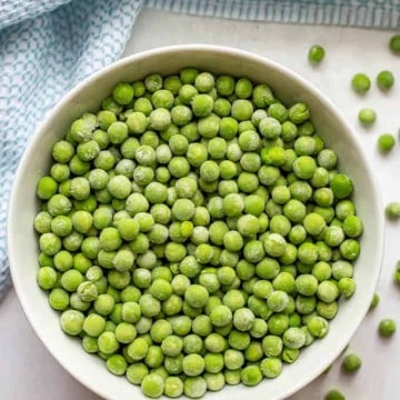 Frozen green peas in a white bowl with extra peas scattered nearby