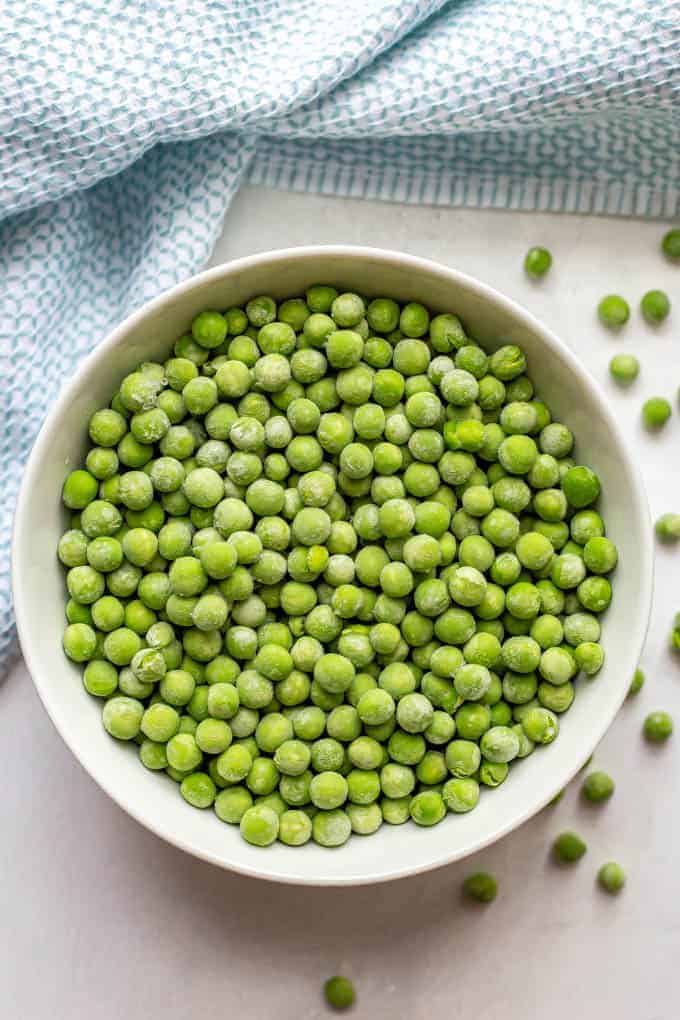 Frozen green peas in a white bowl with extra peas scattered nearby