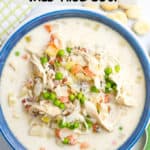 A blue bowl full of a creamy chicken, wild rice and vegetable soup with a spoon to the side.