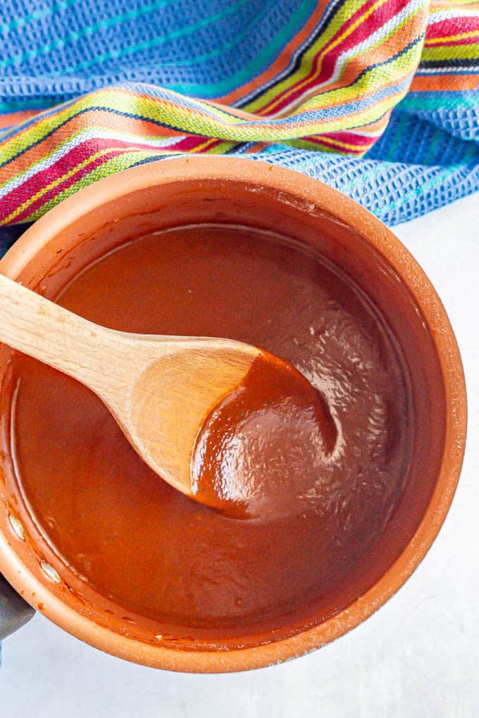 Enchilada sauce in a small copper pot with a wooden spoon resting in it