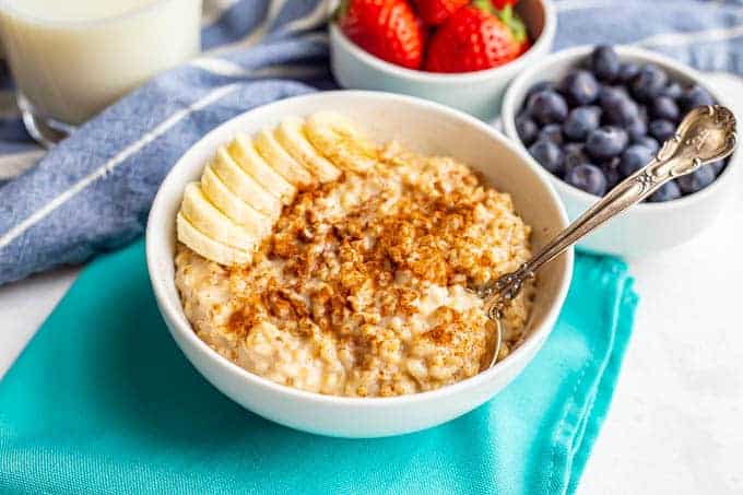 Spoon resting in a bowl of creamy oatmeal with cinnamon sprinkled on top and banana slices in the bowl