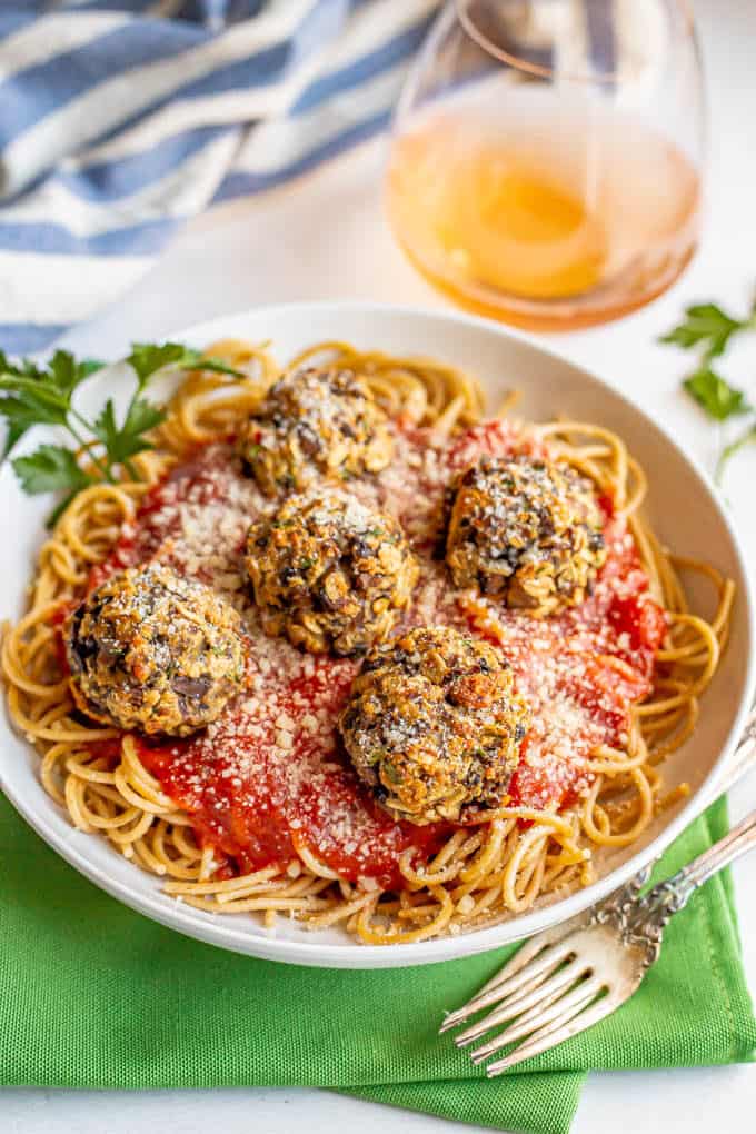 Baked mushroom meatballs served on top of spaghetti and marinara sauce with a glass of rose wine in the background