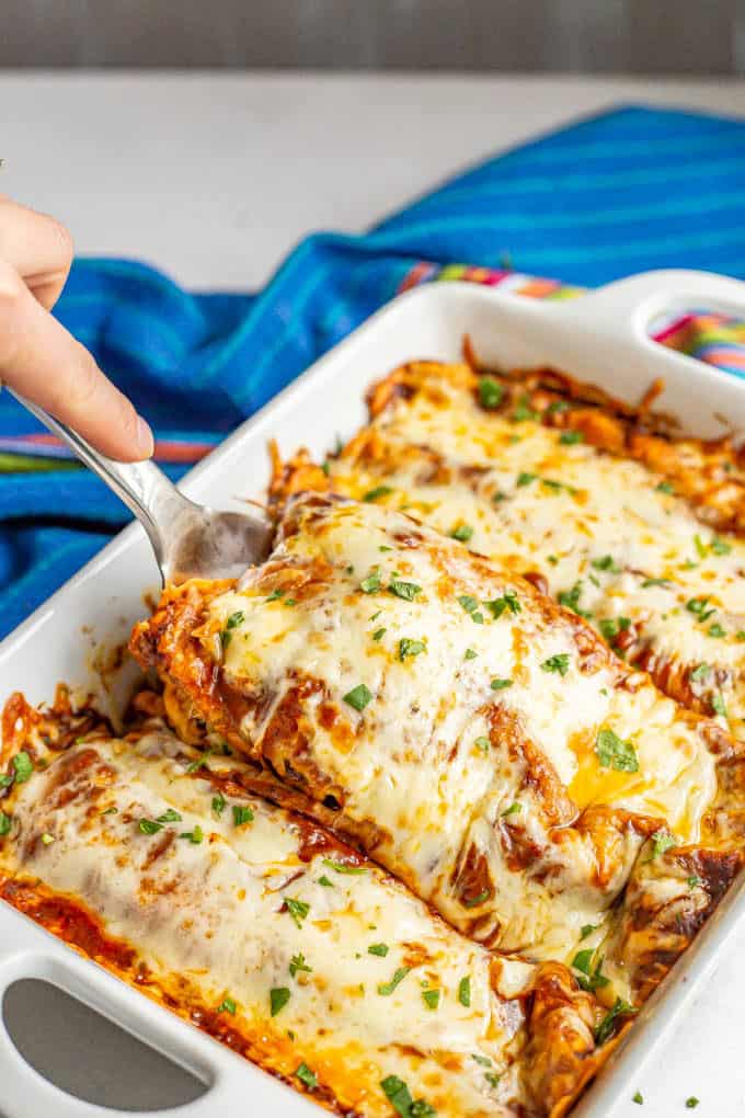Enchiladas being lifted out of a casserole dish after baking
