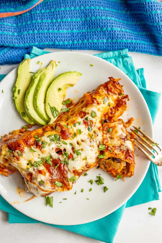Sweet potato black bean enchiladas served on a plate with cilantro and avocado slices