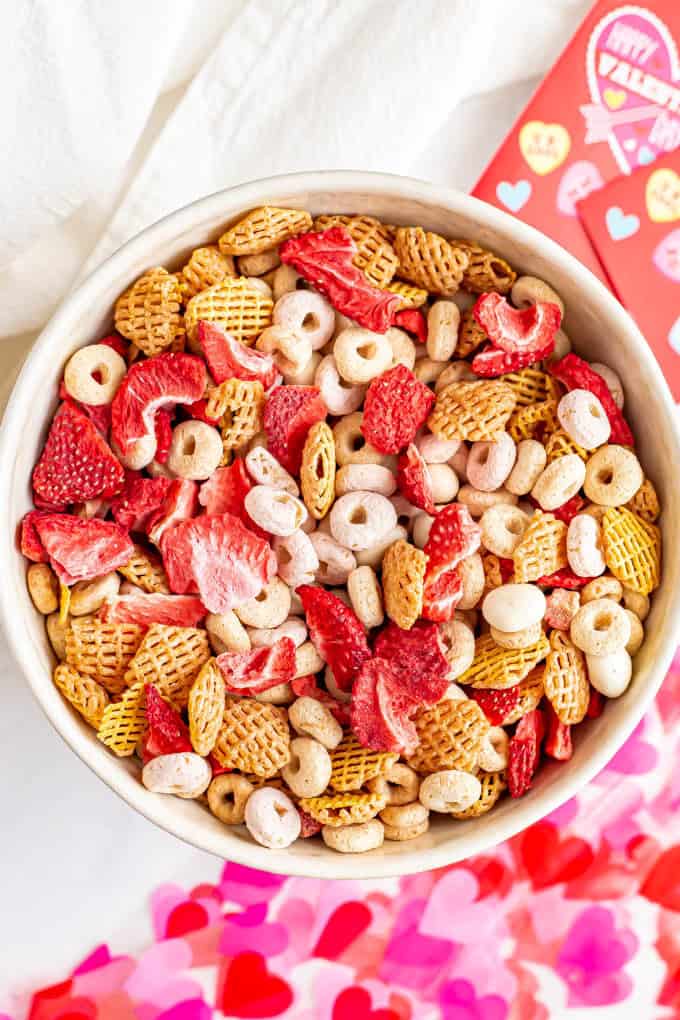 A bowl full of a pink and red colorful Chex mix with cereal and dried strawberries