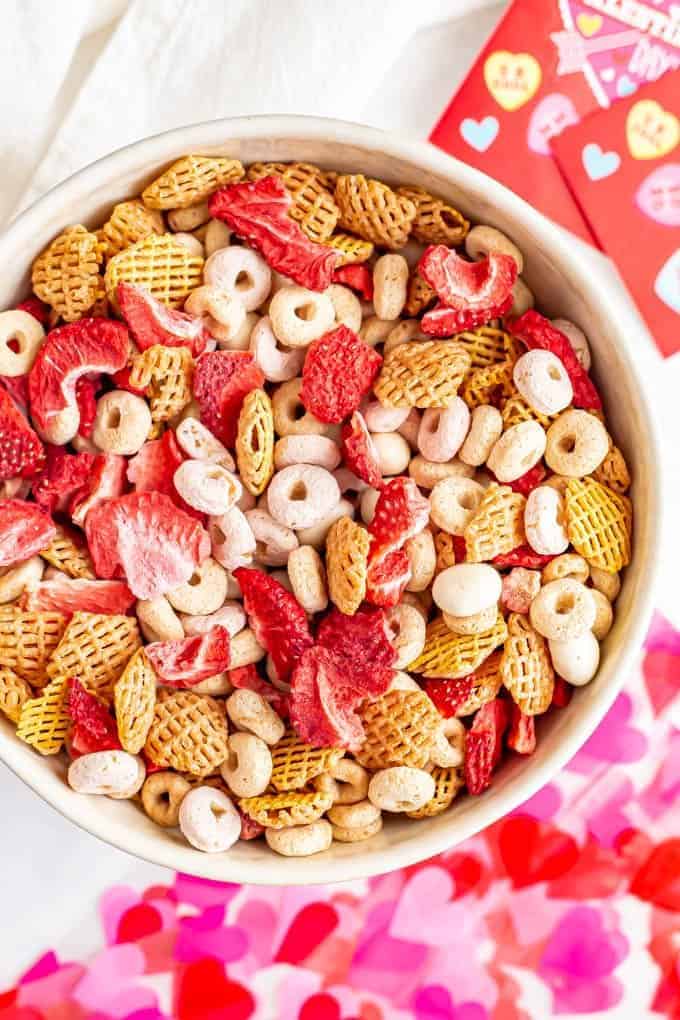A bowl full of a pink and red colorful Chex mix with cereal, dried strawberries and yogurt covered raisins