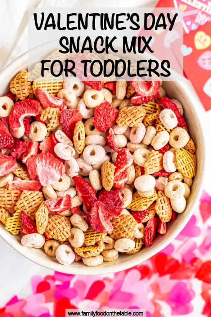 A healthy Valentine's themed snack mix with mixed cereal pieces and dried strawberries and a text overlay on the photo.