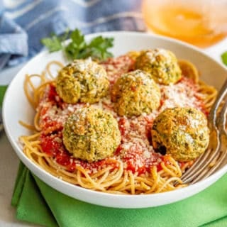 A bowl of spaghetti topped with marinara sauce and vegetarian meatballs with two forks resting in the bowl