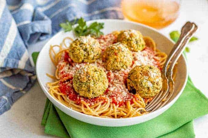 A bowl of spaghetti topped with marinara sauce and vegetarian meatballs with two forks resting in the bowl