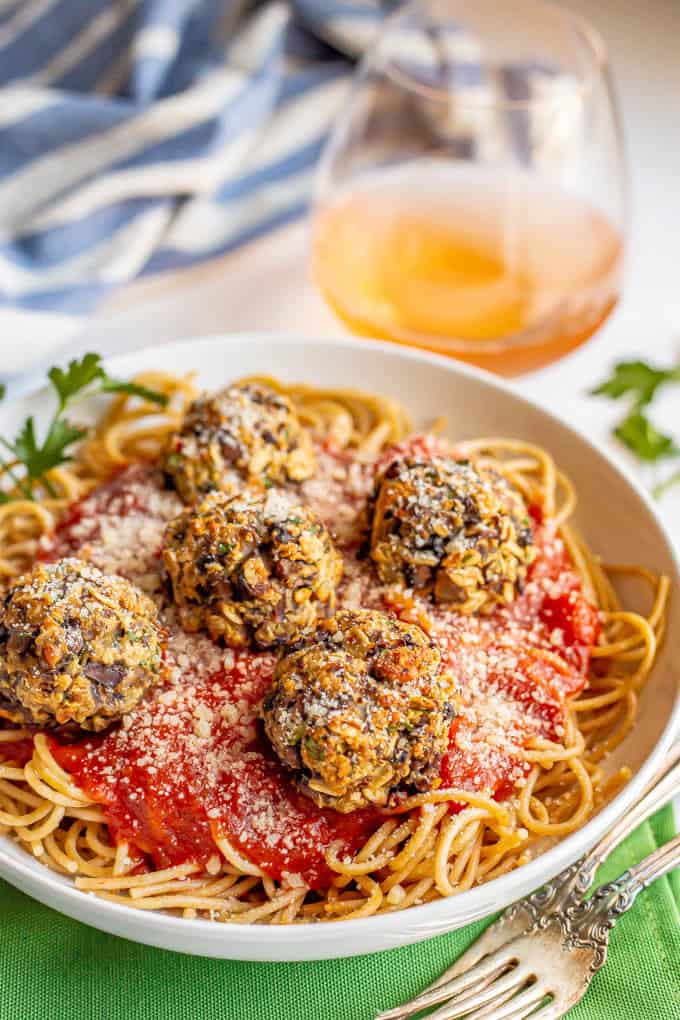 Baked mushroom meatballs served on top of spaghetti and marinara sauce with a glass of rose wine in the background