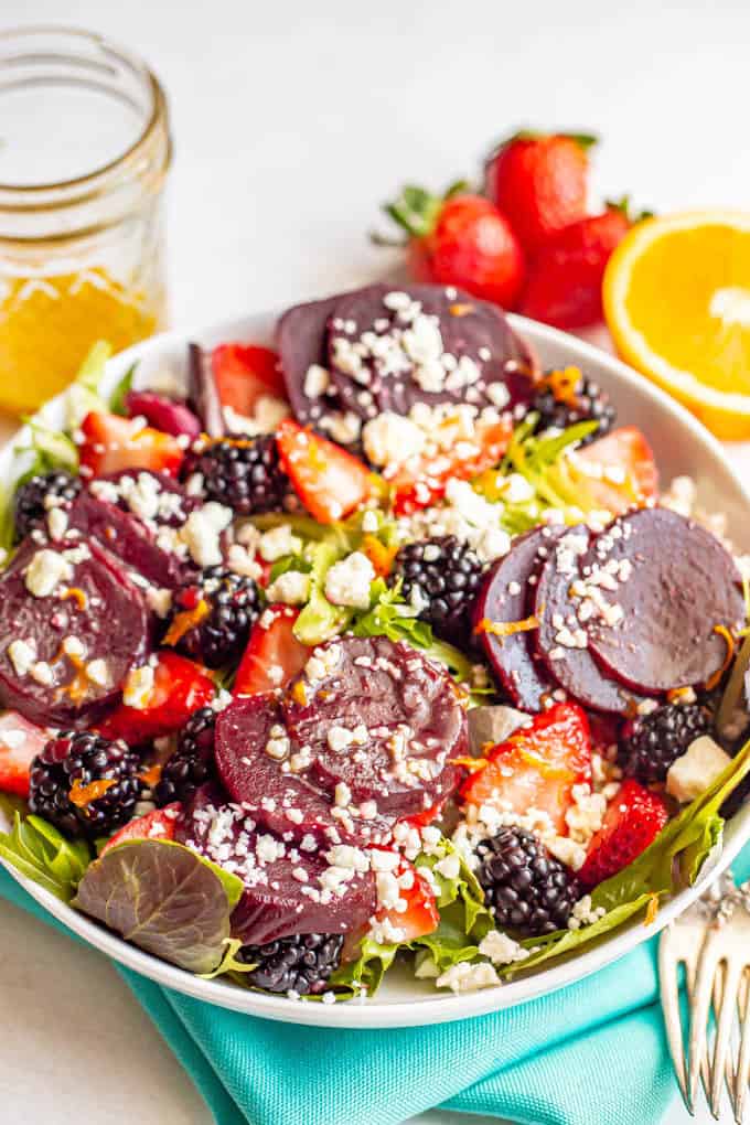 A salad bowl with mixed greens, beets, fresh berries sand feta cheese and a citrus dressing on top