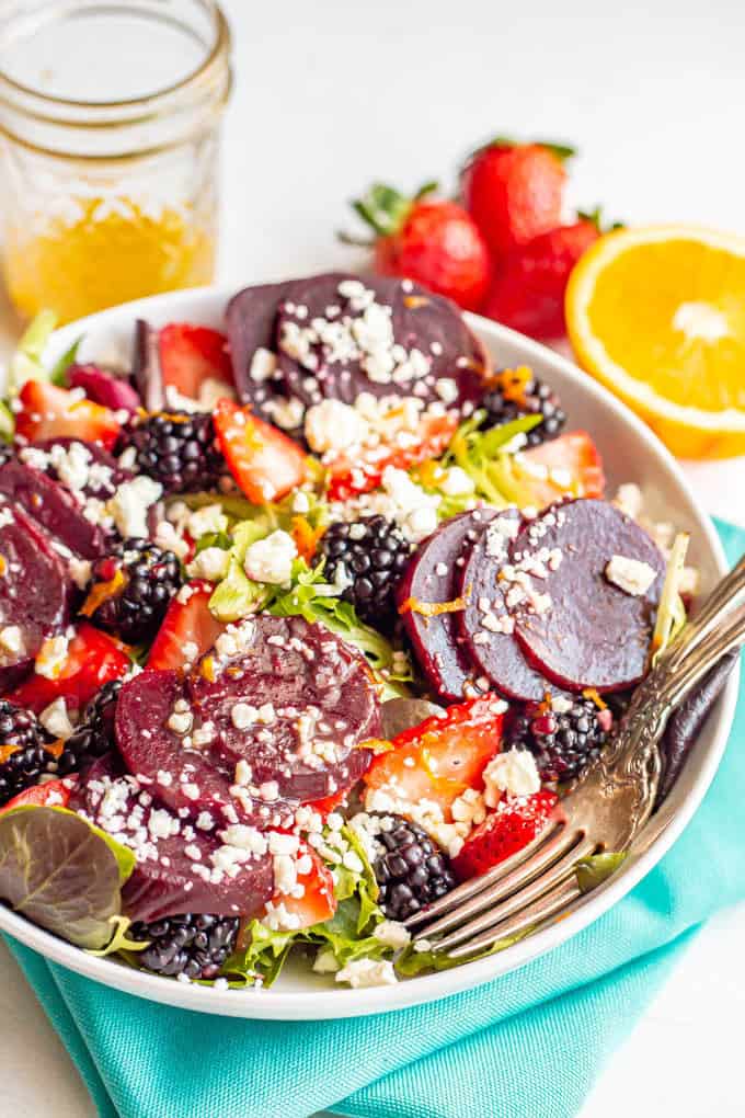 A salad bowl with mixed greens, beets, fresh berries sand feta cheese and two forks tucked in