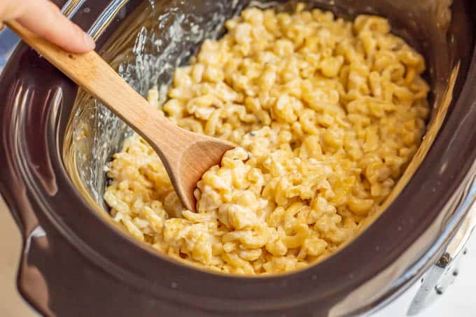 A wooden spoon scooping up some slow cooker mac and cheese after it's cooked