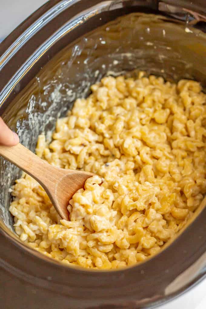 A wooden spoon stirring crock pot mac and cheese after it's cooked