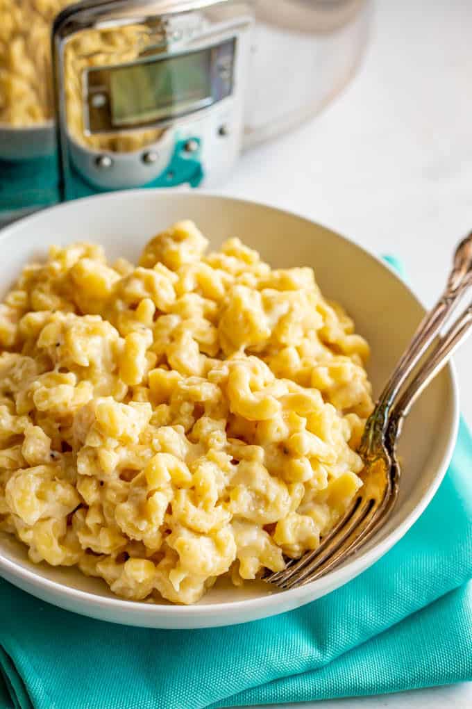 A large serving of macaroni and cheese plated in front of a slow cooker with two forks nestled in the side of the bowl