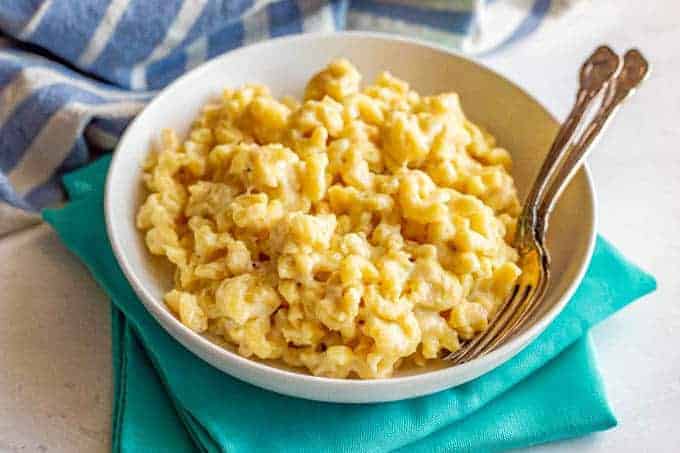 A white bowl served up with macaroni and cheese and two forks