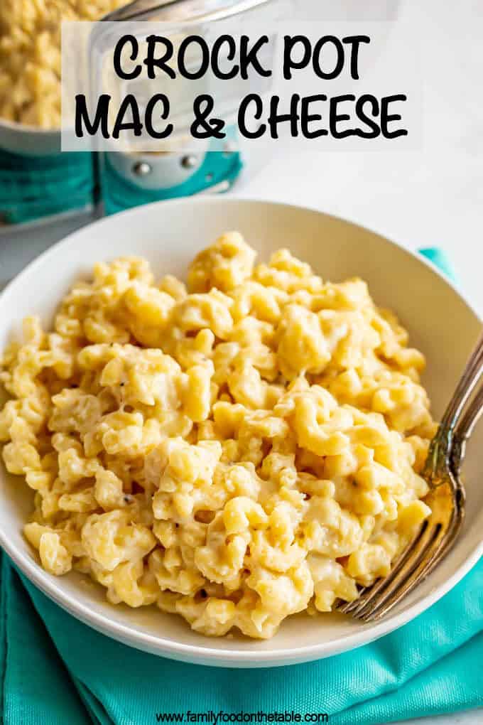 A bowl of creamy mac and cheese in front of a crock pot with two forks in the bowl