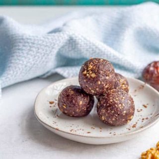 Round chocolate balls made with dates on a white plate with cocoa powder sprinkled over