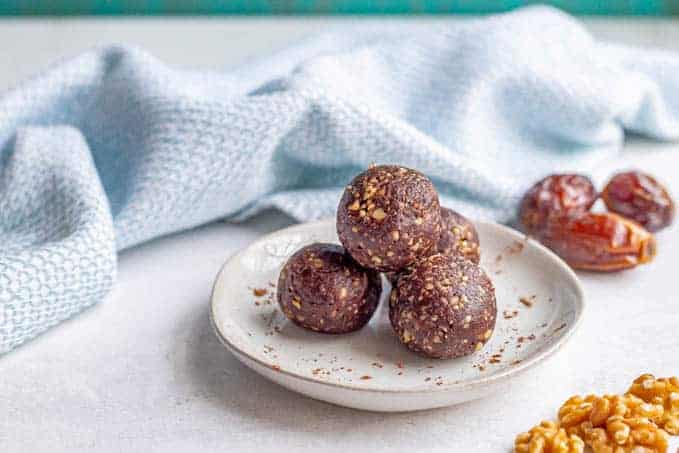 Round chocolate balls made with dates on a white plate with cocoa powder sprinkled over