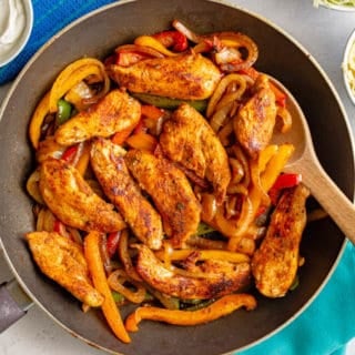 A skillet of cooked chicken and bell peppers with shredded cheese and Greek yogurt nearby
