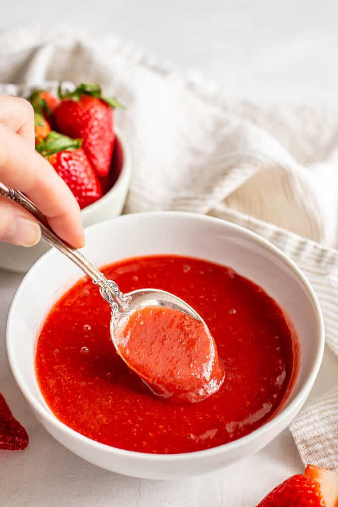 A spoonful of strawberry sauce being taken from a white bowl