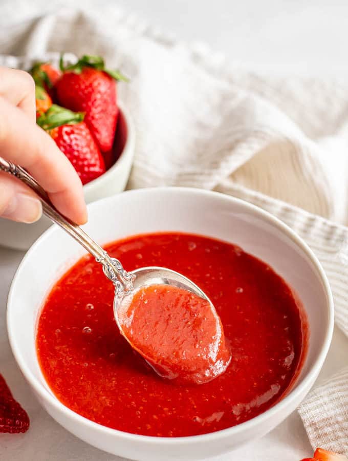 A spoonful of strawberry sauce being taken from a white bowl