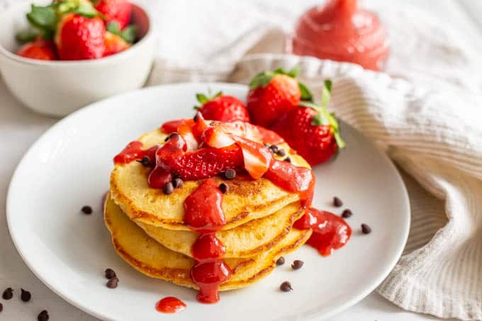 A stack of pancakes with strawberry sauce drizzled over top