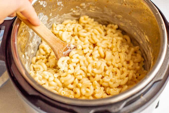 A wooden spoon stirring cooked mac and cheese in a pressure cooker
