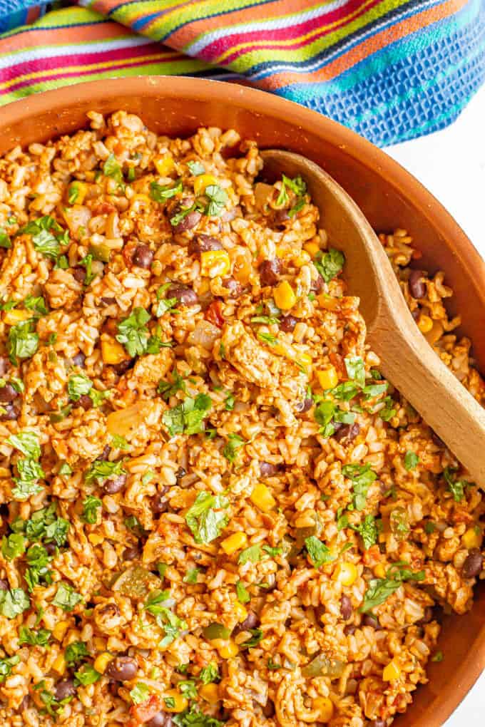 Close up of a wooden spoon in a skillet filled with a ground turkey, rice and bean mixture