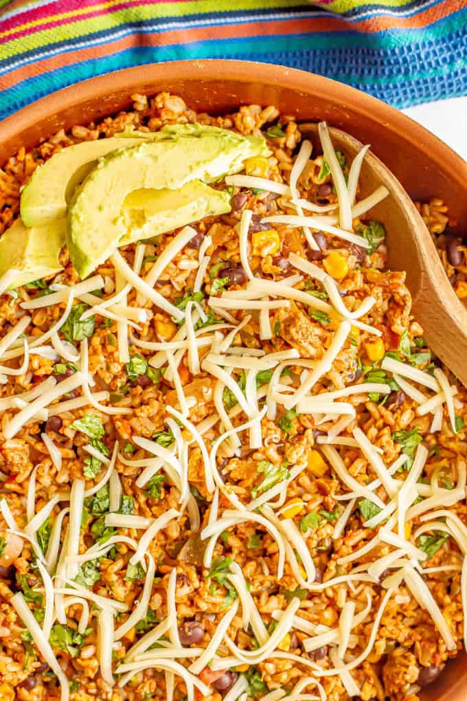 Close up of a Mexican turkey and rice skillet with cilantro, cheese and avocado on top and a wooden spoon resting in the pan