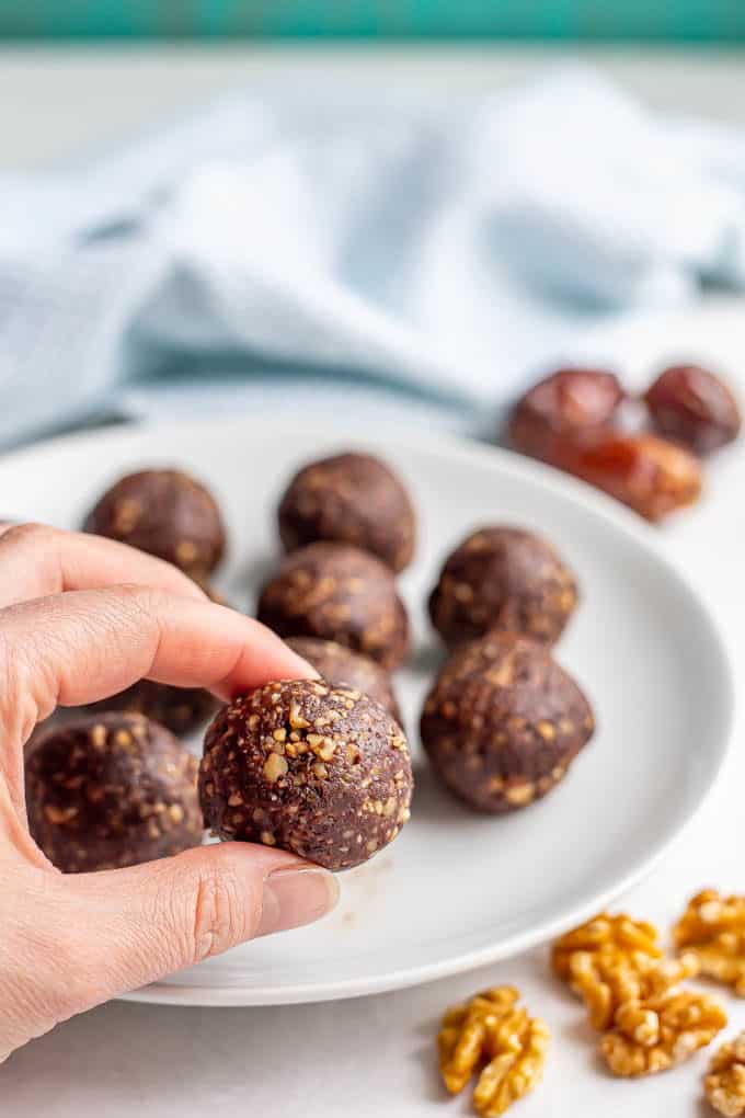 A hand picking up a brownie bite from a plate with walnuts and dates scattered nearby