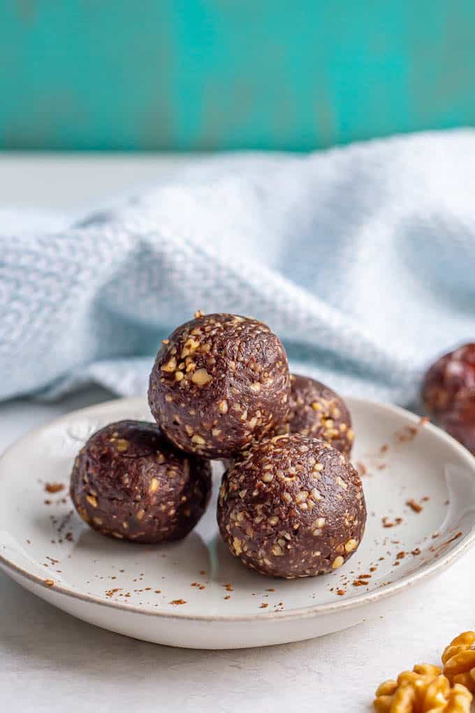 A stack of raw date brownie balls on a plate with a sprinkling of cocoa powder