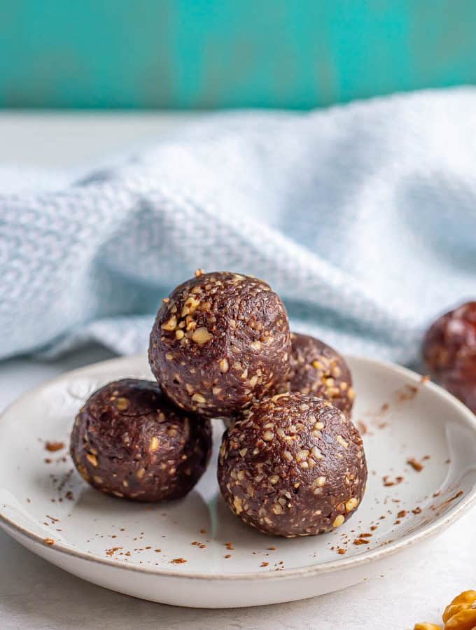 A stack of raw date brownie balls on a plate with a sprinkling of cocoa powder