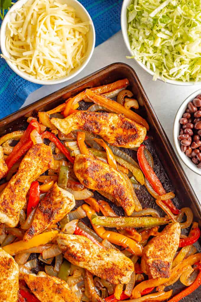Roasted fajita chicken with bell peppers and onions and nearby bowls of toppings