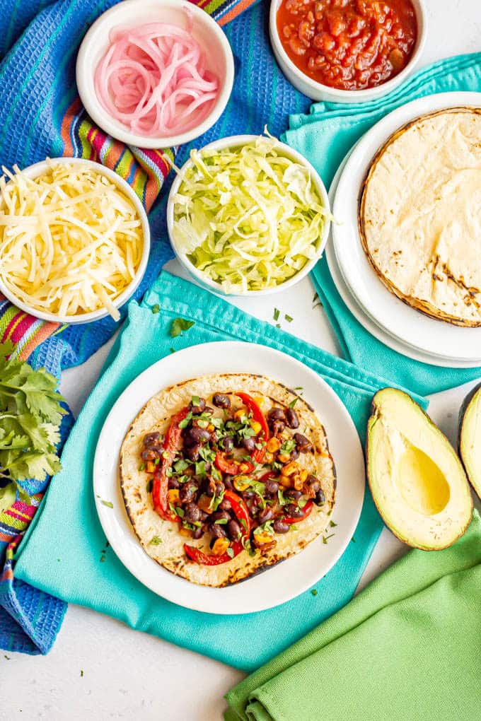 Taco with black beans and vegetables and bowls of toppings nearby